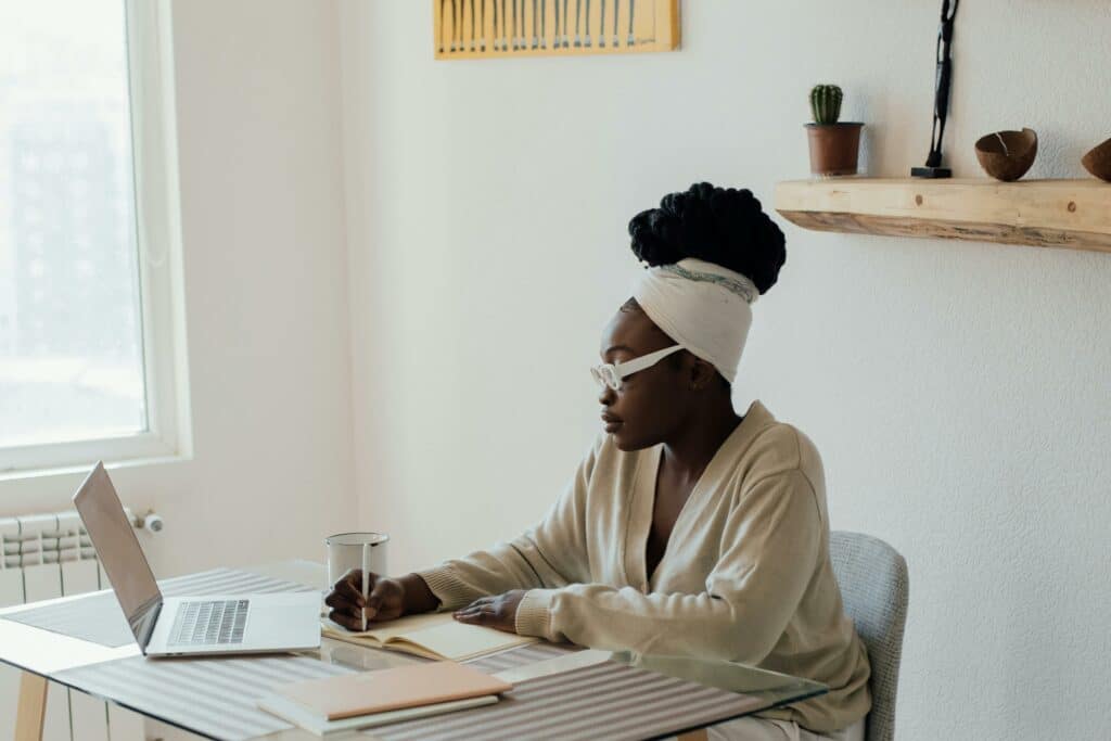 Certified Breastfeeding Counselor Business Tips - black woman with white headwrap sits at desk taking notes by laptop