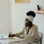 Certified Breastfeeding Counselor Business Tips - black woman with white headwrap sits at desk taking notes by laptop